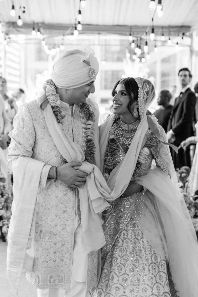 Wedding couple portrait of an indian wedding couple in lehenga and sherwani with floral garlands under indoor string lights amid guests