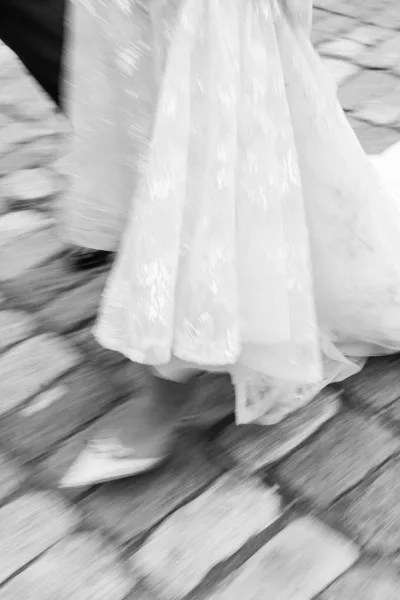 Wedding dress detail with lace wedding dress hem and tulle skirt drifting over pointed bridal heels on stone pavement