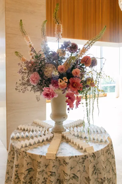 Escort card table with wedding escort cards and a large orchid urn arrangement on linen tablecloth in an indoor venue by tall windows