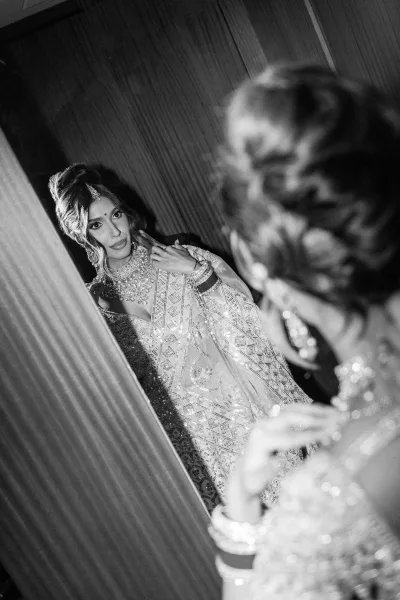 Bridal portrait of a bride in a mirror, wearing an embroidered outfit and statement necklace, against a wood-paneled wall indoors