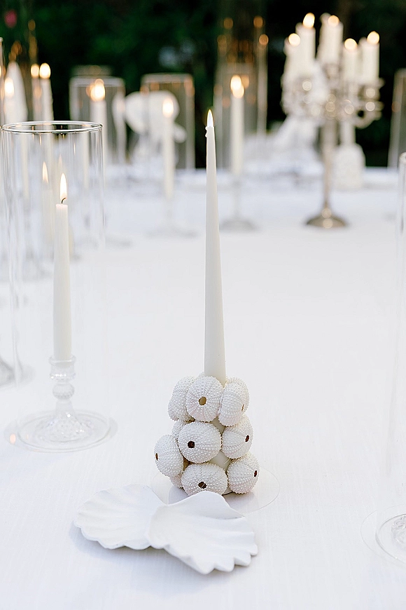 Wedding tablescape with white wedding table decor, taper candles and silver candelabra, ceramic shell dishes, and soft greenery bokeh in back