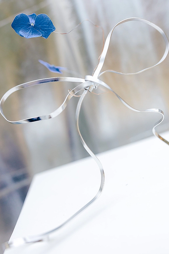 Wedding boutonniere featuring a blue flower with a silver ribbon accent, pinned neatly against a white surface with a soft blurred backdrop