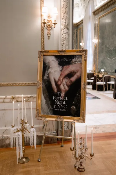 Wedding welcome sign in a gold frame on an easel, flanked by taper candles with dripping wax in an ornate ballroom entrance
