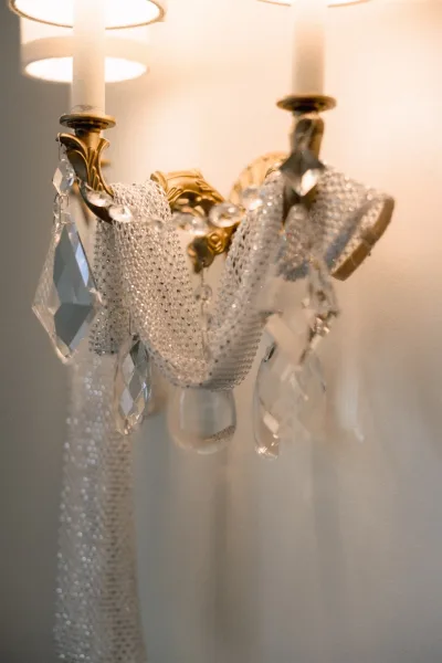 Wedding chandelier decor with crystal chandelier wedding decor, gold arms, taper candles, and hanging prisms glowing against a white wall