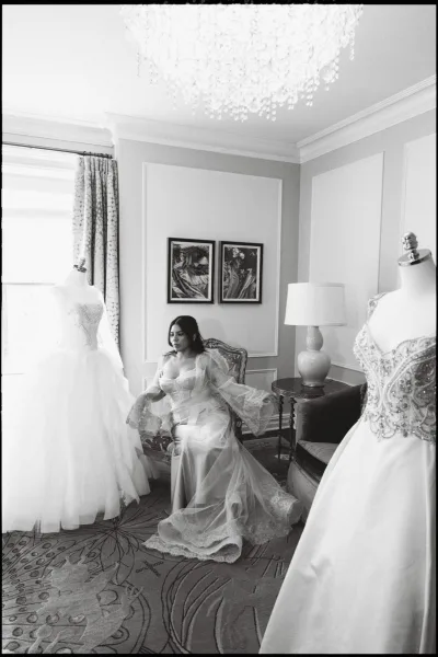 Bridal portrait of a bride sitting in an upholstered chair in window light, wearing a satin slip dress with a bridal veil in a paneled living room