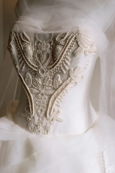 Wedding dress close-up showing lace wedding dress bodice with intricate beadwork and embroidery on a neutral backdrop