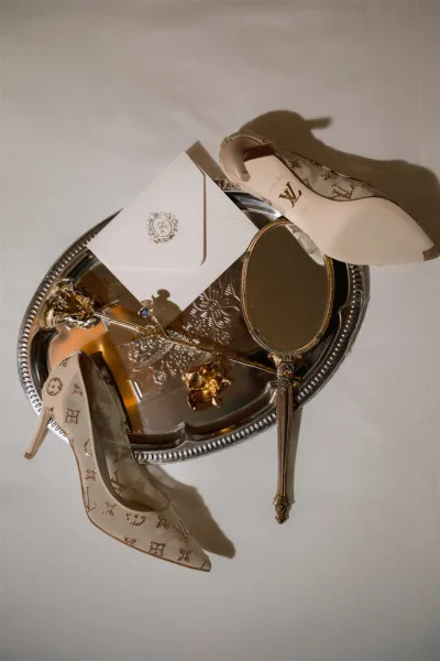 Wedding flat lay bridal detail flat lay with heels, invitation envelope, blue sapphire engagement ring, hand mirror, and gold pins on white surface