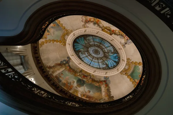 Grand staircase ceiling in an ornate wedding venue interior, looking up to a stained glass skylight over mural and plaster molding