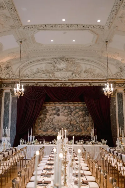 Reception tablescape on a long banquet table wedding with taper candles and candelabras, white linens, gold chairs, in an ornate marble hall
