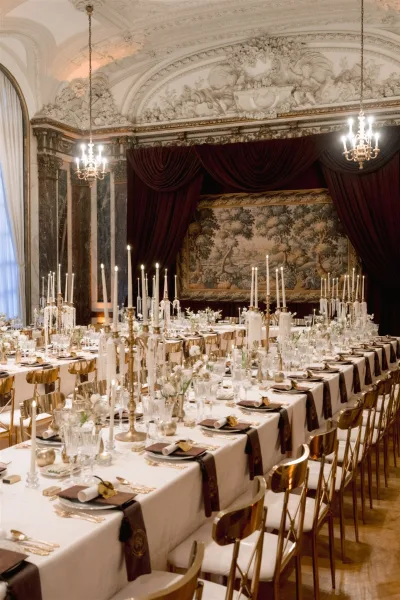 Reception tablescape on a long banquet table wedding with taper candles and crystal glassware under chandeliers in an ornate ballroom
