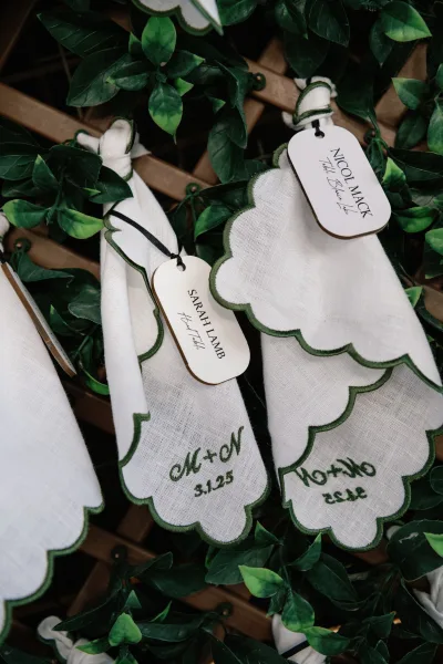 Wedding place cards hanging in an escort card display on black string with greenery garland against a wooden lattice backdrop