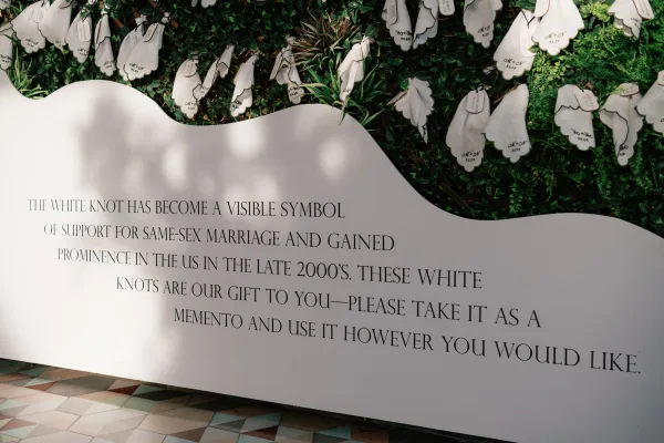 Wedding signage wedding welcome sign on a greenery wall with white board, hanging favor tags and escort cards, sunlit tile floor