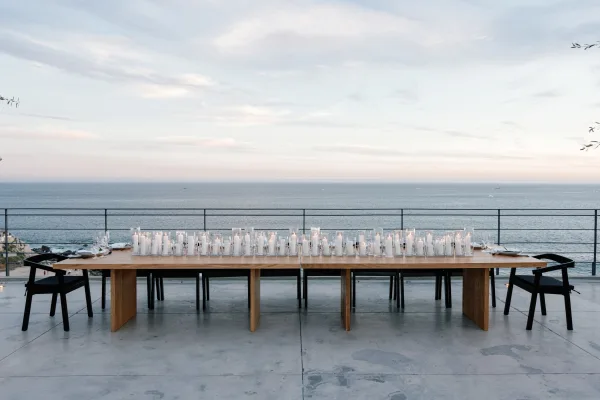 Reception tablescape with a long banquet table wedding setup, white taper candles in glass holders on a terrace with ocean view