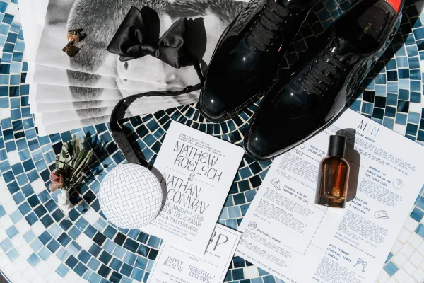 Invitation suite with modern wedding invitations arranged on blue mosaic tile, with black bow tie, shoes, cufflinks, and cologne