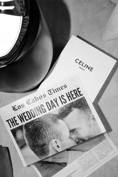 Wedding newspaper and newspaper wedding program set on a tabletop, with printed card tucked in an envelope beside a lamp