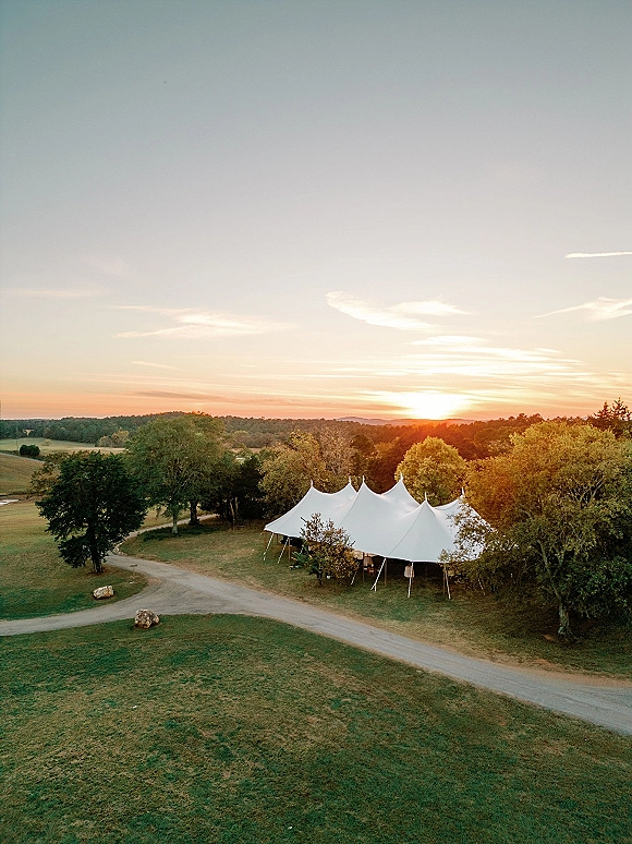 Outdoor reception tent, a white sailcloth wedding tent with poles and stakes in an open field at sunset with trees and distant hills