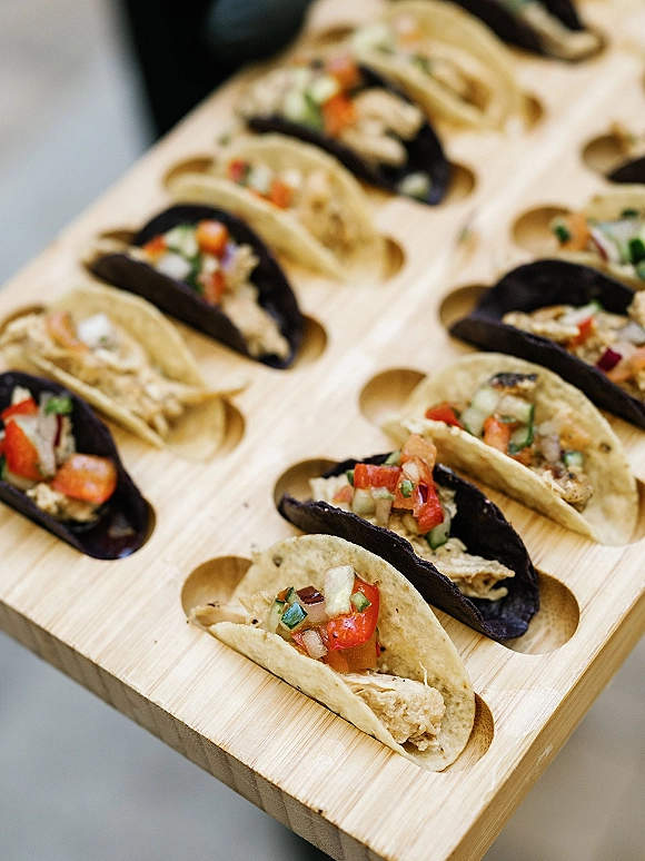 Wedding taco appetizers arranged in a wooden taco holder, mini tacos filled with toppings and pico de gallo on a catering tray