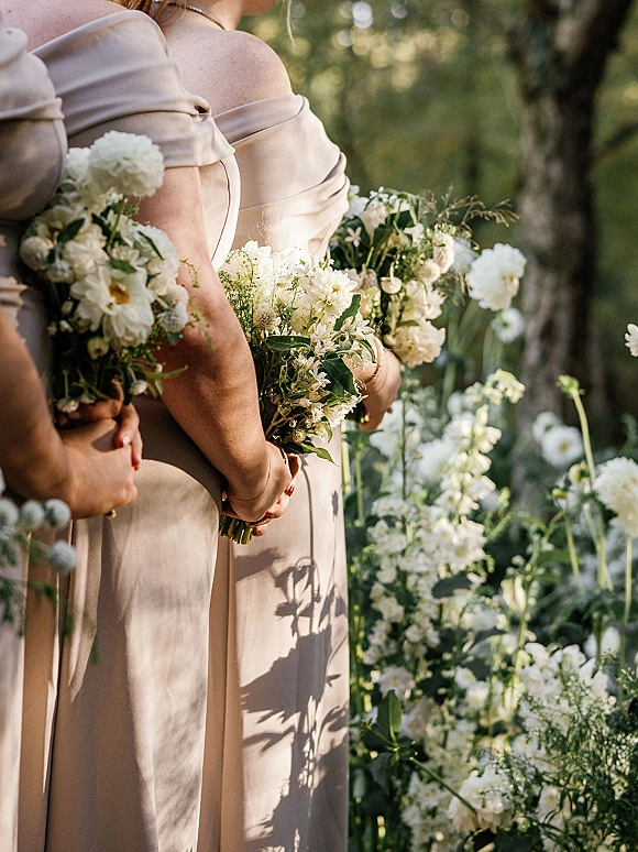 Bridesmaid bouquets of white wildflowers and greenery held by bridesmaids in champagne off-the-shoulder dresses in a garden setting