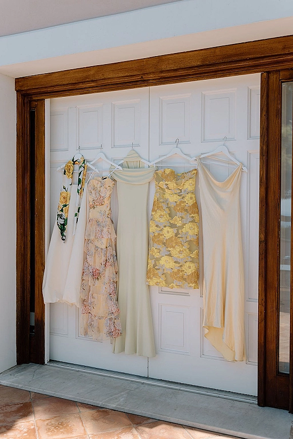 Bridesmaid dresses hanging in a bridesmaid dress lineup on white paneled doors, featuring floral print, gold brocade, and a scarf accent