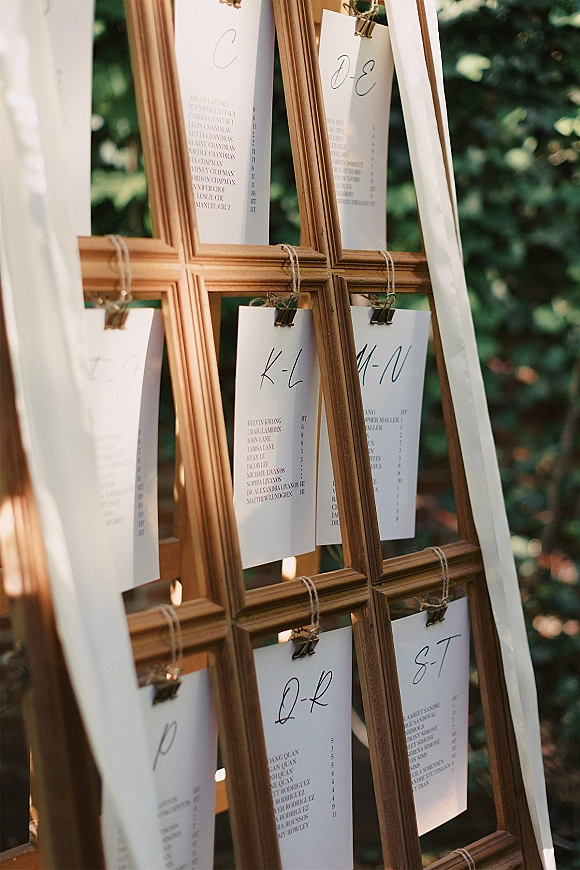 Wedding seating chart seating chart display with white cards clipped to twine on a wood frame easel, calligraphy lettering in outdoor greenery