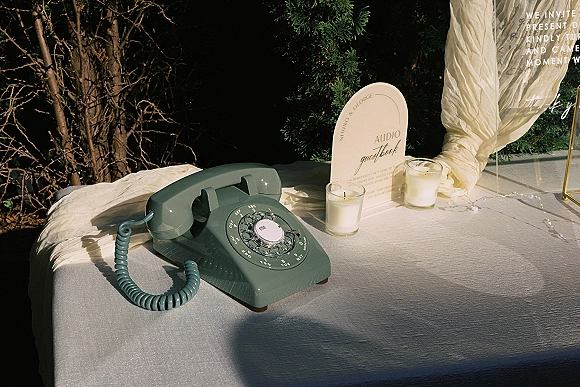 Wedding audio guestbook with an audio guestbook phone, vintage rotary handset on a candlelit table with string lights in sunlit greenery