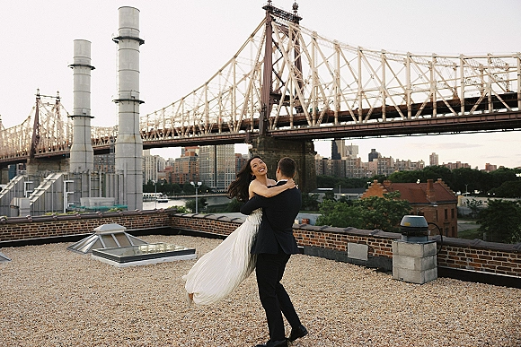 Couple portrait of groom spinning his bride in a strapless wedding dress, rooftop wedding photos with bridge and city skyline over the river
