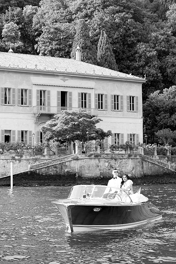 Couple portrait on a motorboat, boat wedding photo with bride in fur stole and groom in sunglasses, gliding past a waterfront villa