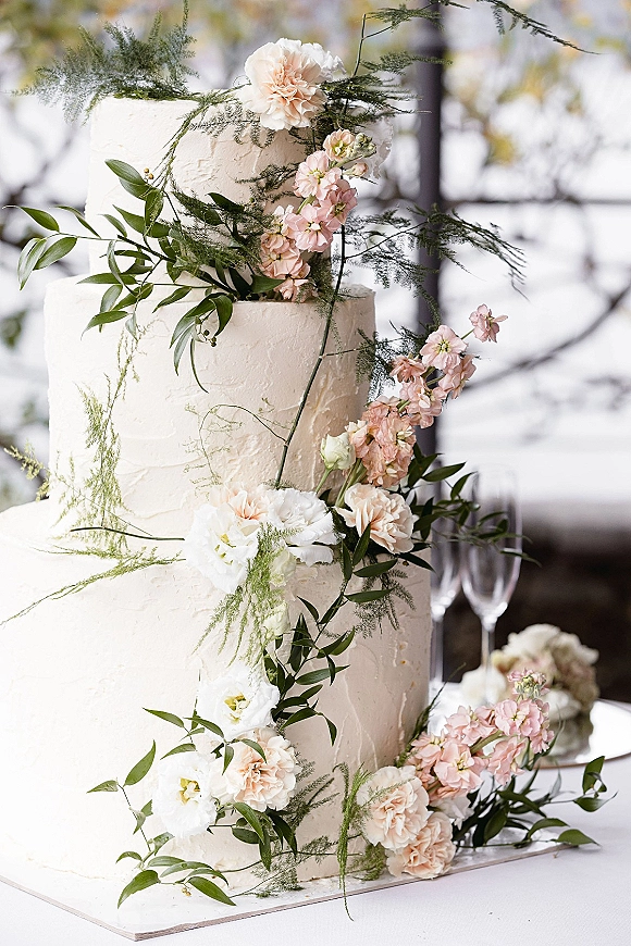 Wedding cake three tier wedding cake with textured white buttercream, blush and white flowers, and trailing greenery by window light