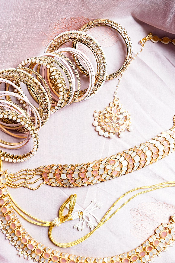 Bridal jewelry flatlay featuring indian bridal jewelry with kundan choker, pendant necklace, and gold-pearl bangles on blush pink fabric folds