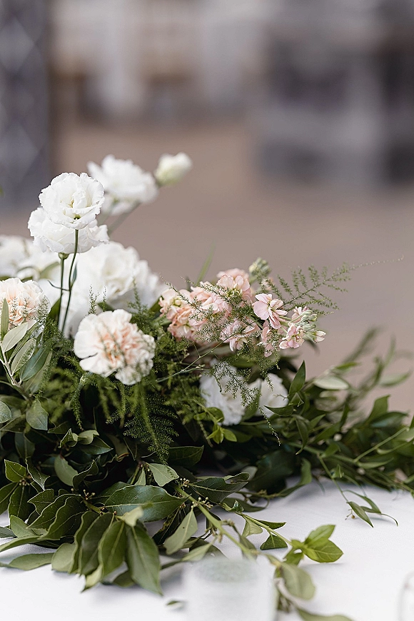 Wedding bouquet with white and blush bouquet blooms and trailing greenery, captured close up against a softly blurred outdoor pavement backdrop