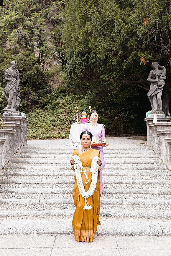 Bridal entrance with an Indian wedding entrance as the bride descends stone steps in a sari, jasmine garland and gold jewelry amid garden greenery