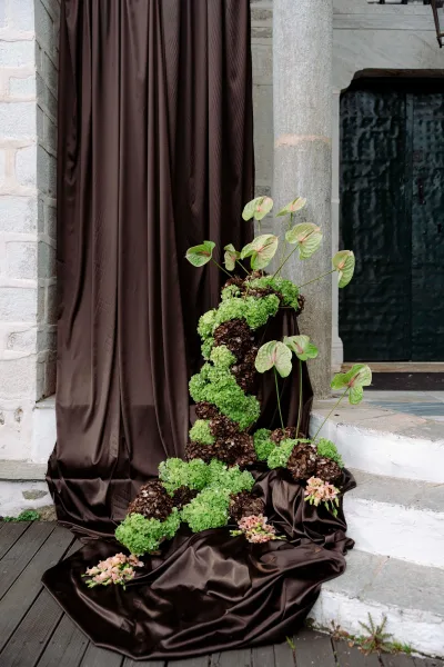 Ceremony entrance decor with wedding draped backdrop, chocolate brown fabric and hydrangea floral installation on stone steps by a black door