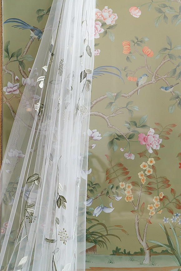 Bridal veil with embroidered wedding veil floral embroidery on tulle draped against a painted floral mural wallpaper with birds and blossoms