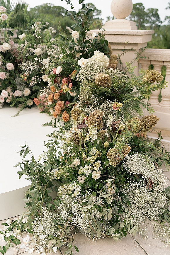 Wedding ceremony florals with a ground floral arrangement of roses, hydrangea and greenery, accented by scattered rose petals on a terrace patio