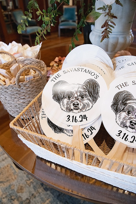 Wedding program fans with custom wedding fan programs featuring illustrated dog artwork and printed date, arranged in a wicker basket on a wooden table