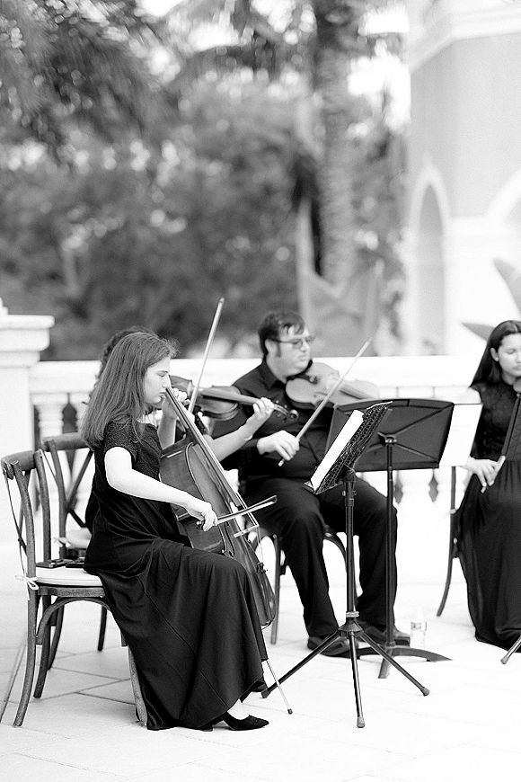 Wedding musicians in black attire perform as a wedding string quartet with cello and violins on an outdoor terrace by a white balustrade
