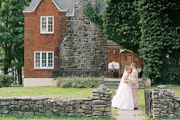 Wedding couple portrait of the bride and groom kiss as she holds a bouquet beside an ivy-covered brick and stone building entrance