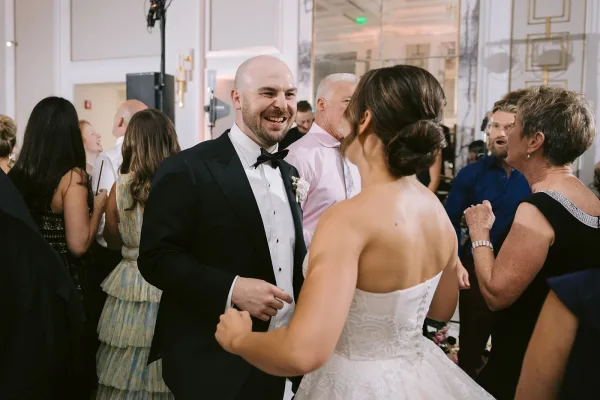 Wedding reception dancing as bride in a strapless lace wedding dress spins with groom in tuxedo on a ballroom dance floor, guests cheering nearby