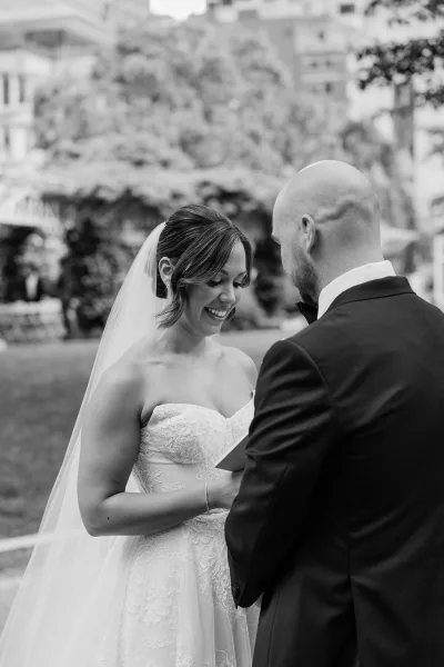 Wedding vows as the bride reads to her groom, smiling in a strapless lace dress and veil during an outdoor wedding ceremony in a garden