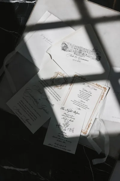 Invitation suite with classic wedding invitations, RSVP and details cards wrapped in vellum ribbon on black marble with window-light shadows