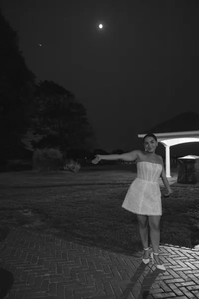 Bridal portrait of a bride in a short wedding dress with sparkling strapless corset, arms out on a lawn under the moonlit night sky