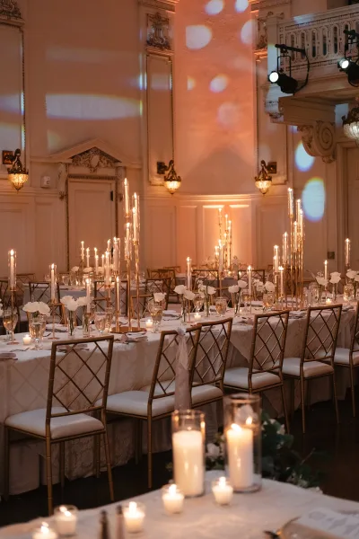 Reception tablescape with candlelit wedding reception glow, tall taper candles, white florals, and gold chairs in an ornate ballroom with chandelier