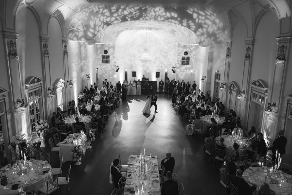 First dance in a black and white wedding reception as bride in gown and groom in tuxedo twirl under chandelier in a grand ballroom