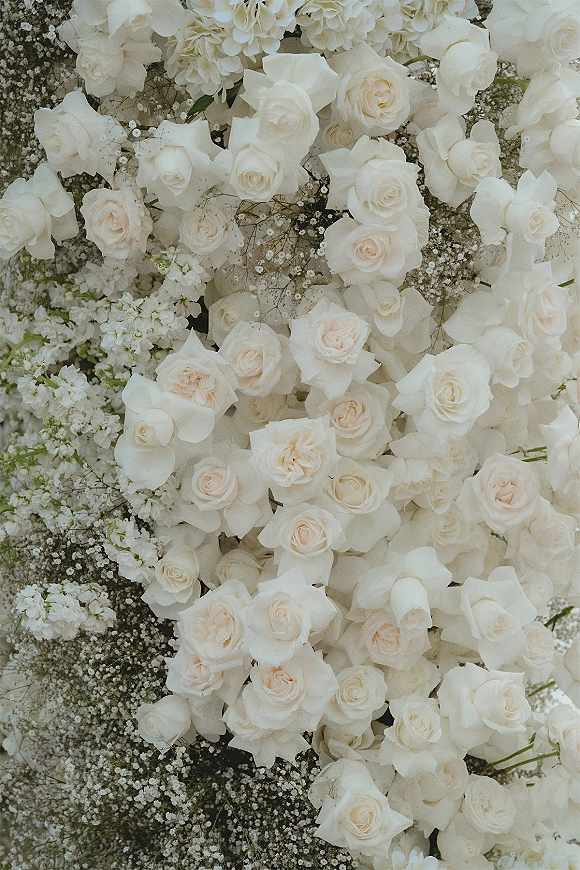 Wedding floral arrangement with white rose wedding flowers and baby's breath, lush greenery, displayed against a full floral backdrop