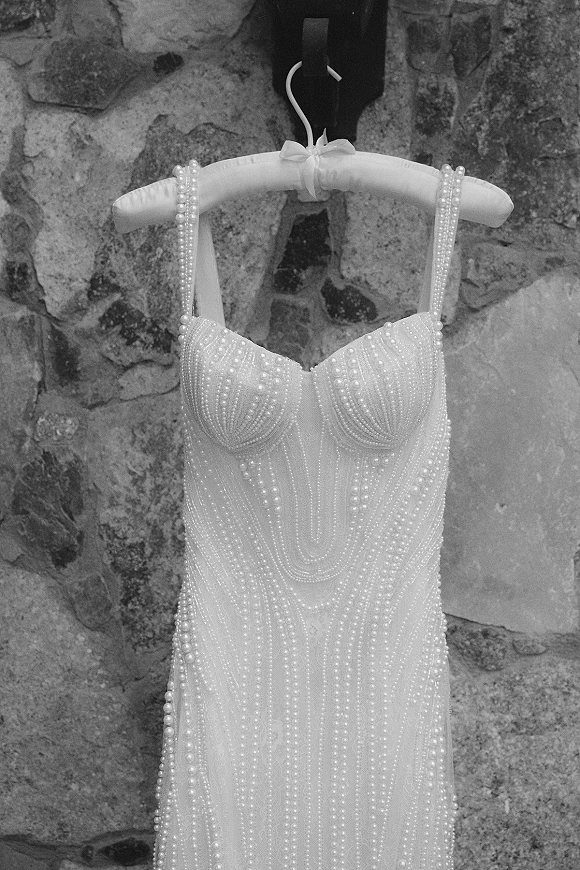 Wedding dress close-up of a pearl wedding dress with spaghetti straps and sweetheart neckline on a padded hanger against a stone wall