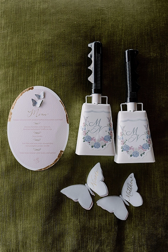 Wedding reception details with an oval wedding menu card featuring gold-edged paper, butterfly place cards, and monogram labels on green linen