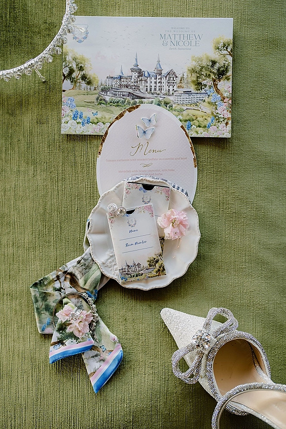 Invitation suite with watercolor wedding invitation, oval menu and place cards styled with glitter heels on green textured fabric