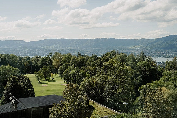 Wedding venue view overlooking a mountain wedding venue with lake, forest trees, golf course lawn, and cloudy sky from a rooftop perspective