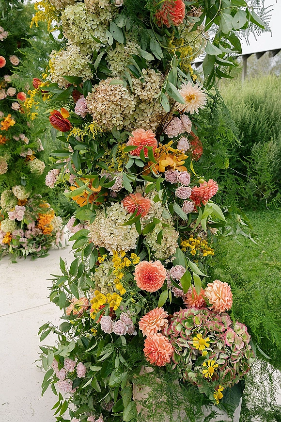 Wedding floral arch with hydrangeas, dahlias, and roses in an asymmetrical floral arch, framed by garden trees and lush greenery garland