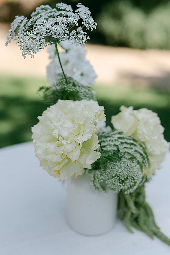 Wedding centerpiece with white hydrangea centerpiece blooms, Queen Anne's lace, and greenery in a white vase on a table outdoors on lawn walkway